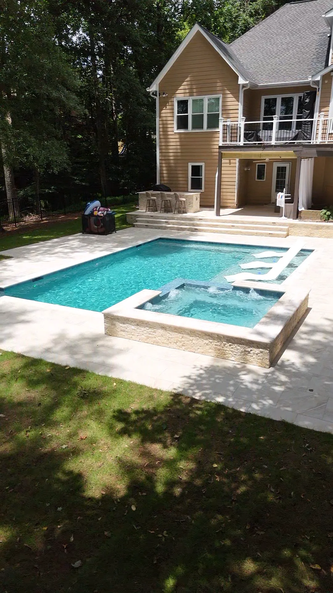 Wide view of a finished backyard pool and raised spa in front of a two-story home