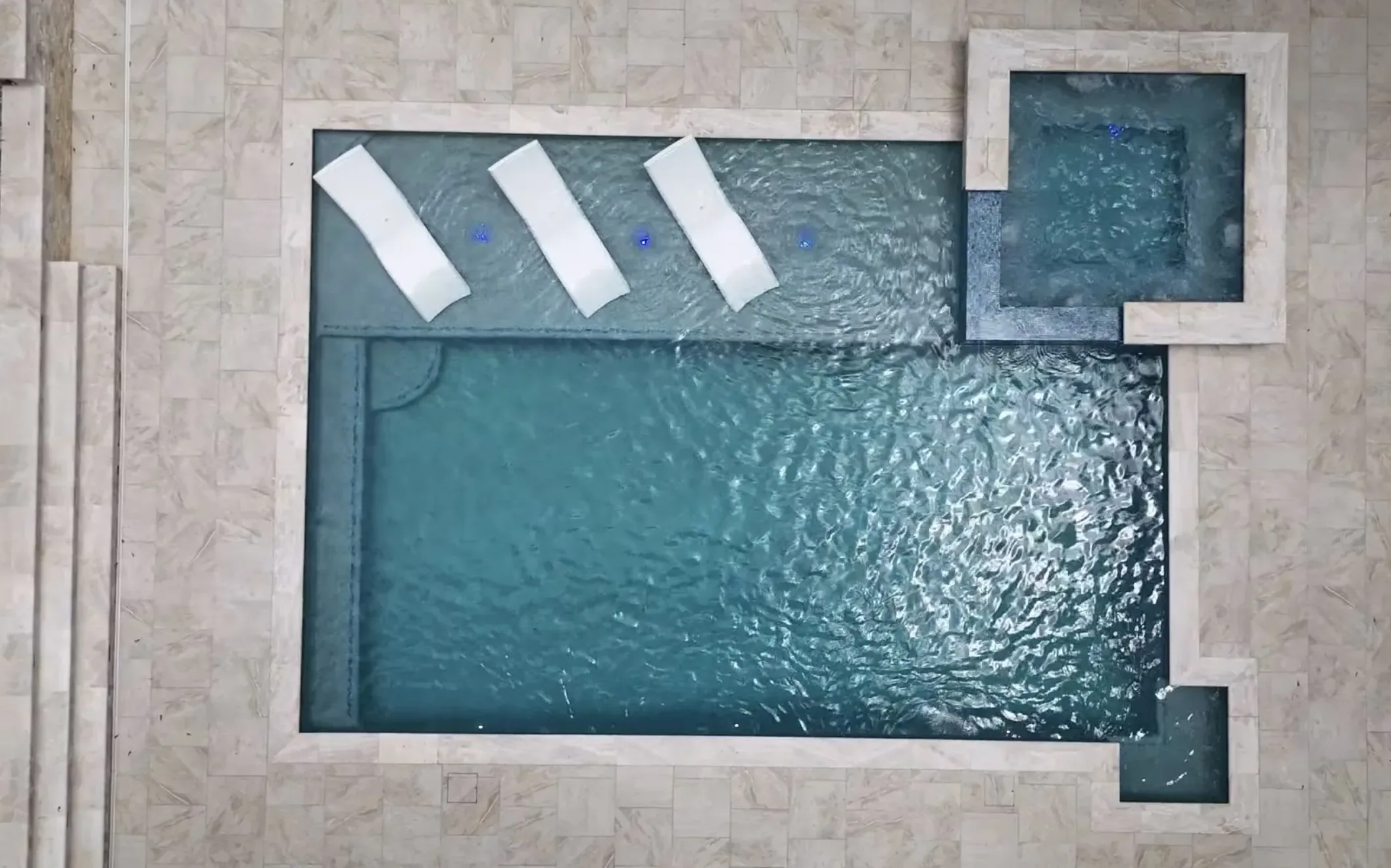 Straight-down drone view of a raised spa and in-water loungers beside the main pool