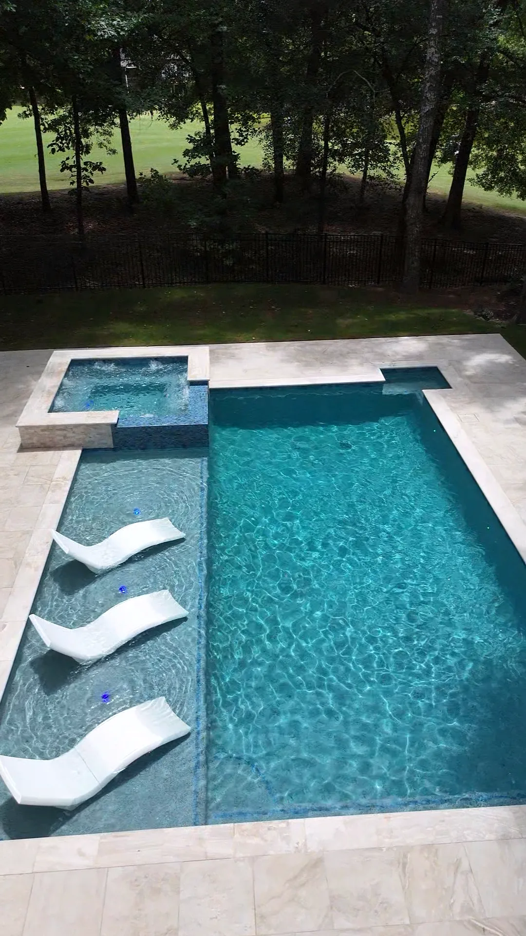 Angled overhead view of a raised spa with in-water loungers and the pool beside it