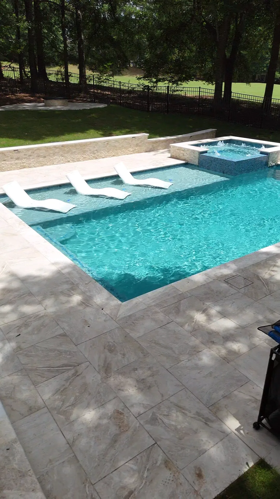 Elevated view of a raised spa and pool framed by trees along the property line