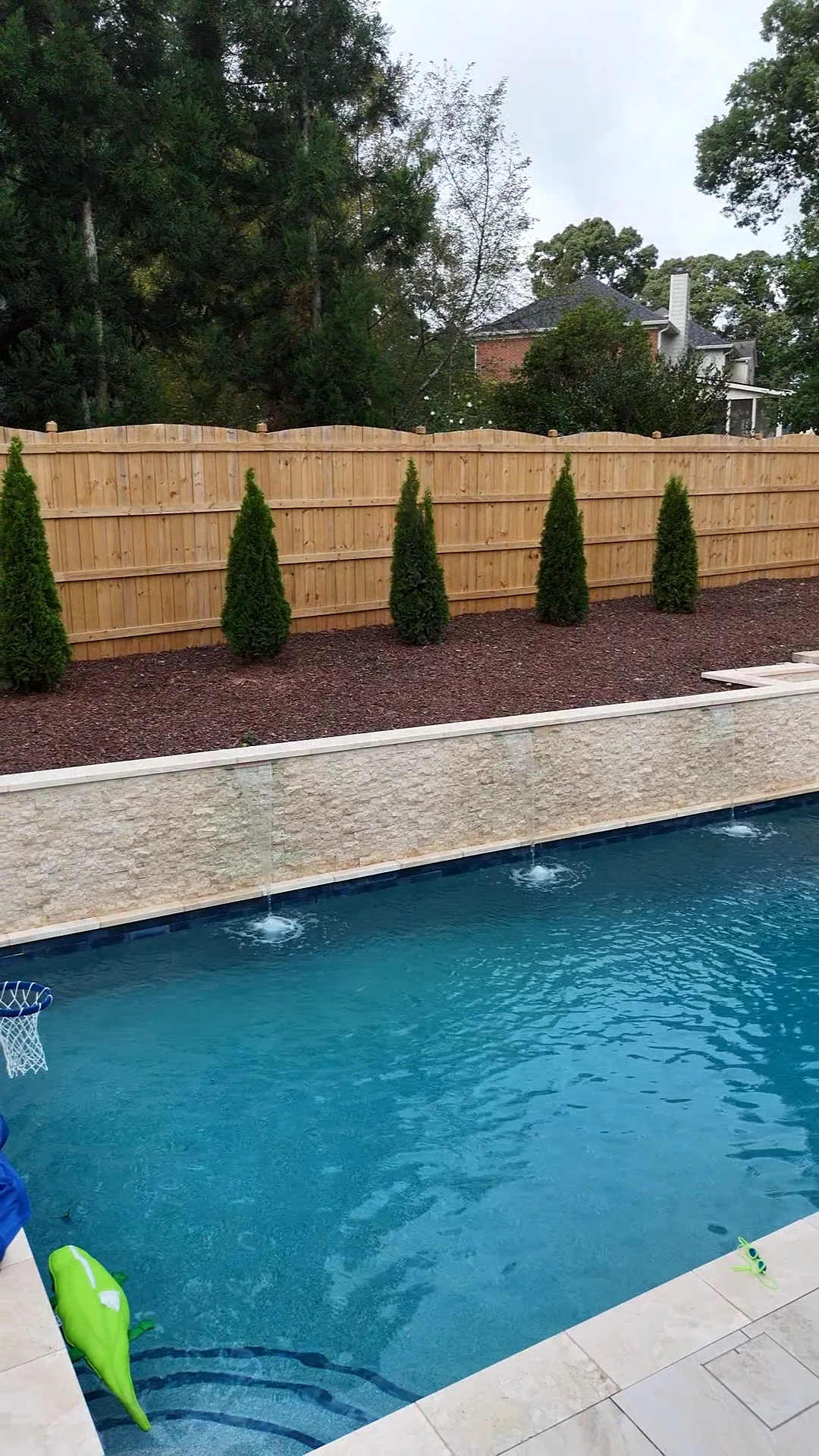 Three-spout sheer-descent water wall into the pool beside newly planted arborvitae landscaping