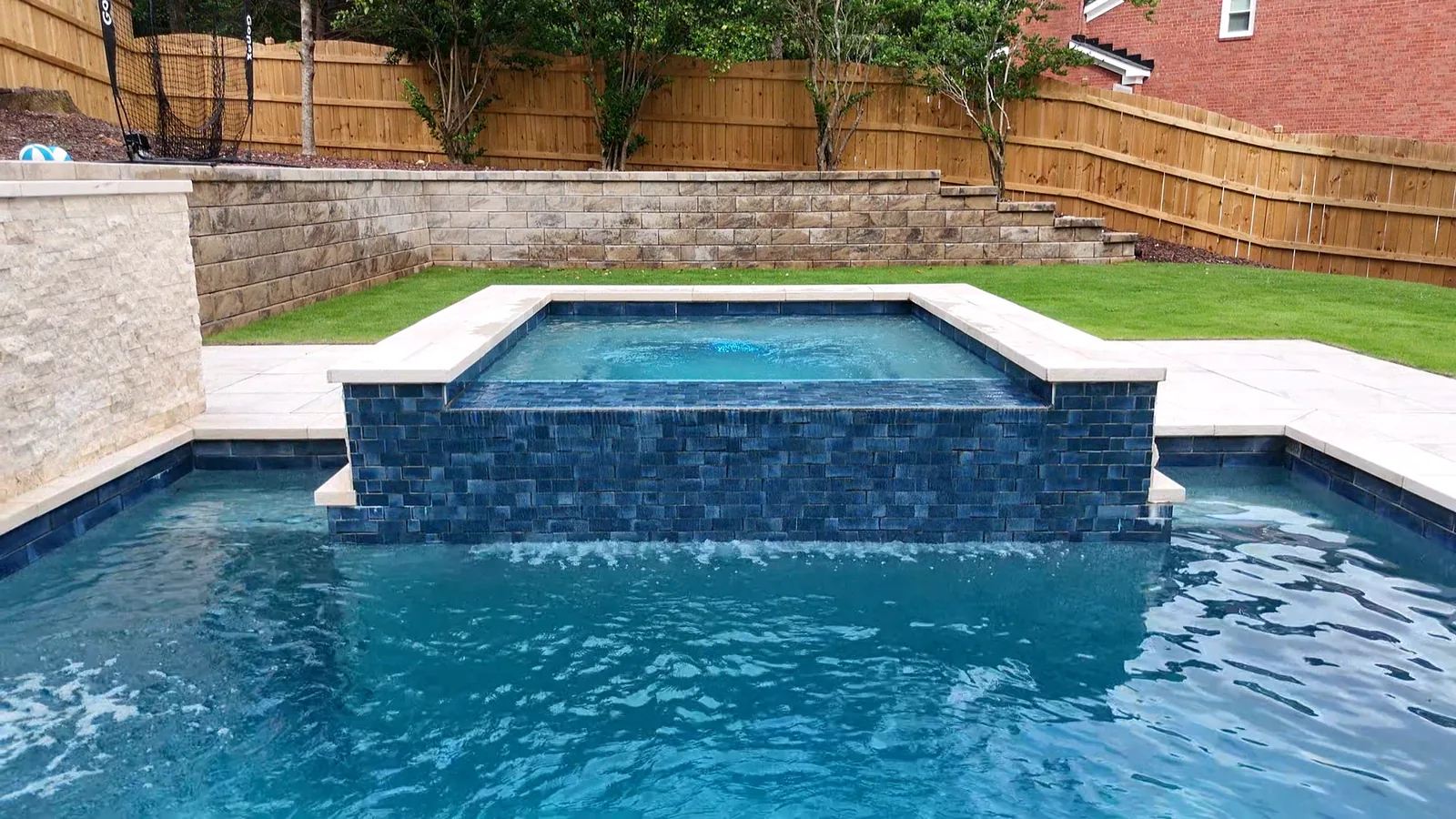 Sheer-descent water feature spilling over a dark tiled wall into a finished pool