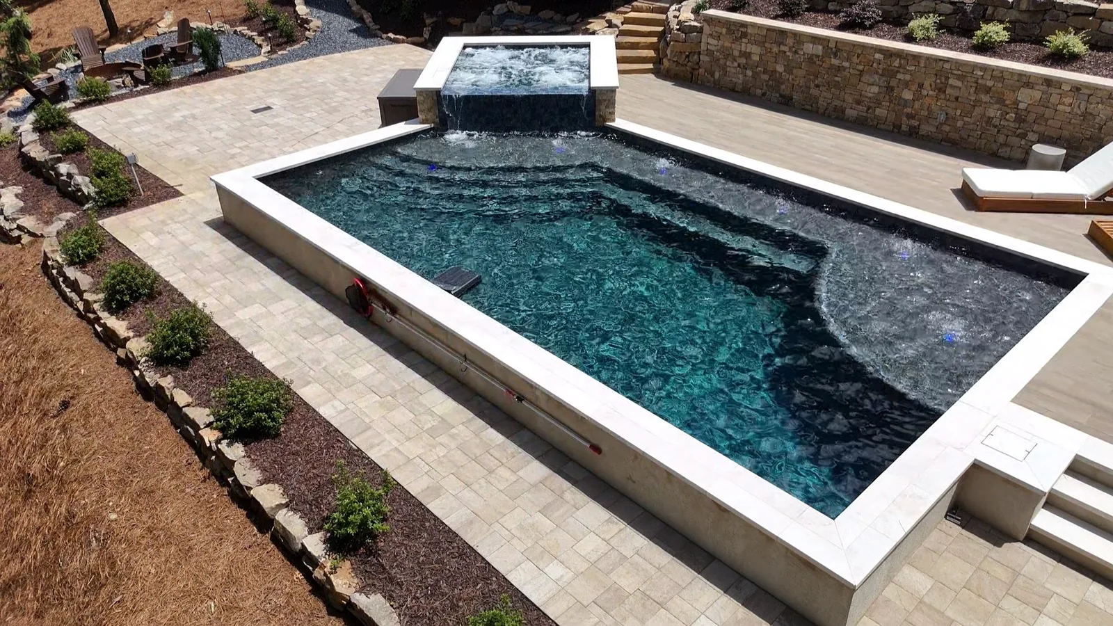 Elevated view of a pool and raised spa with a lounge patio and a fire-pit seating area in the background