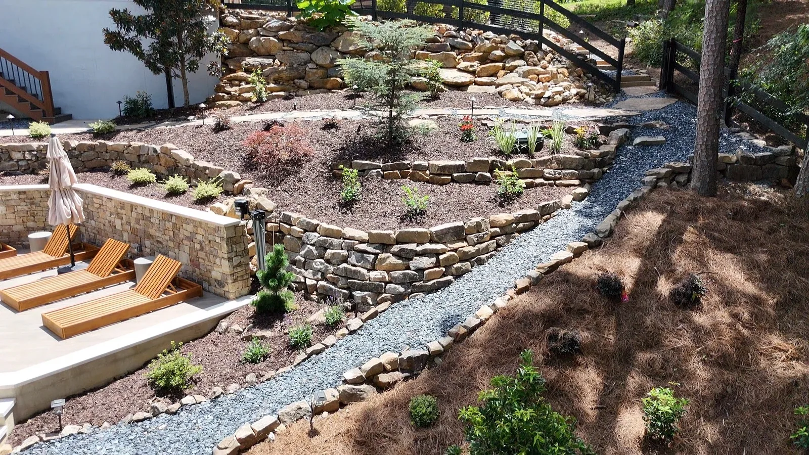 Terraced dry-creek stone hardscape and landscaping climbing the hillside beside the patio