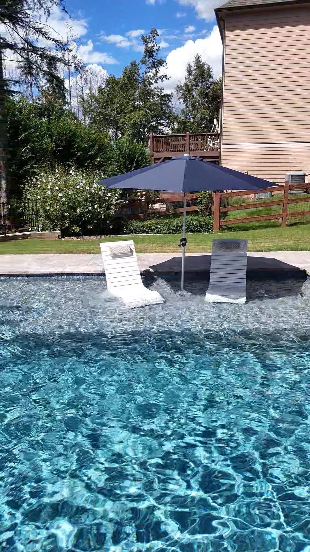 Two white in-water loungers under a dark umbrella in the finished Dallas pool