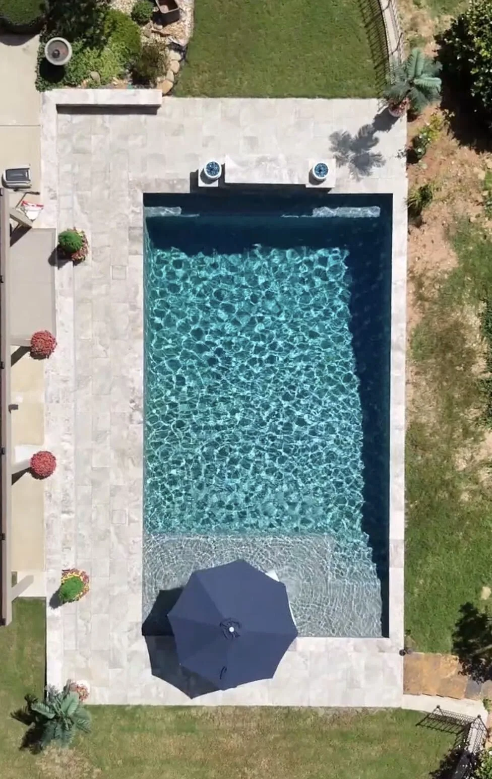 Overhead view of the Dallas pool, pale patio, waterfall wall and umbrella on the shallow ledge