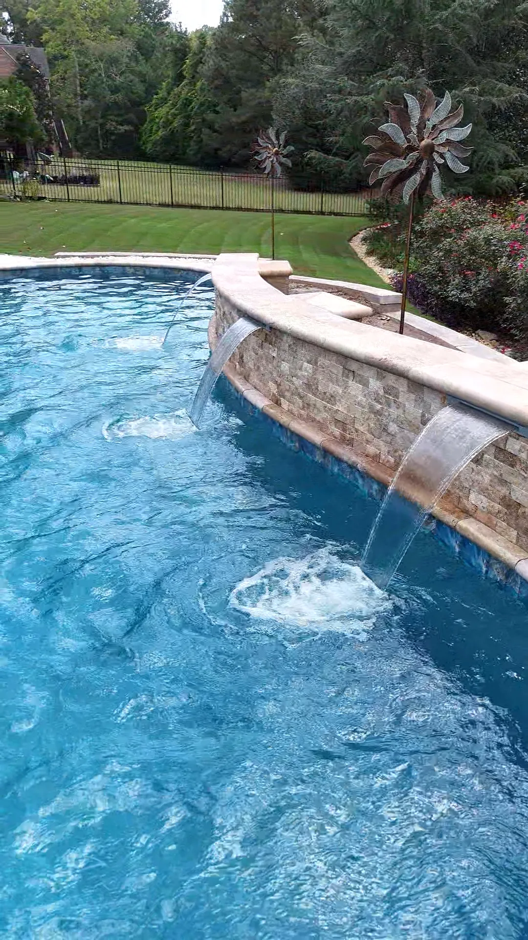 Close view of two water features flowing from the Curtis project's curved stone wall into the pool