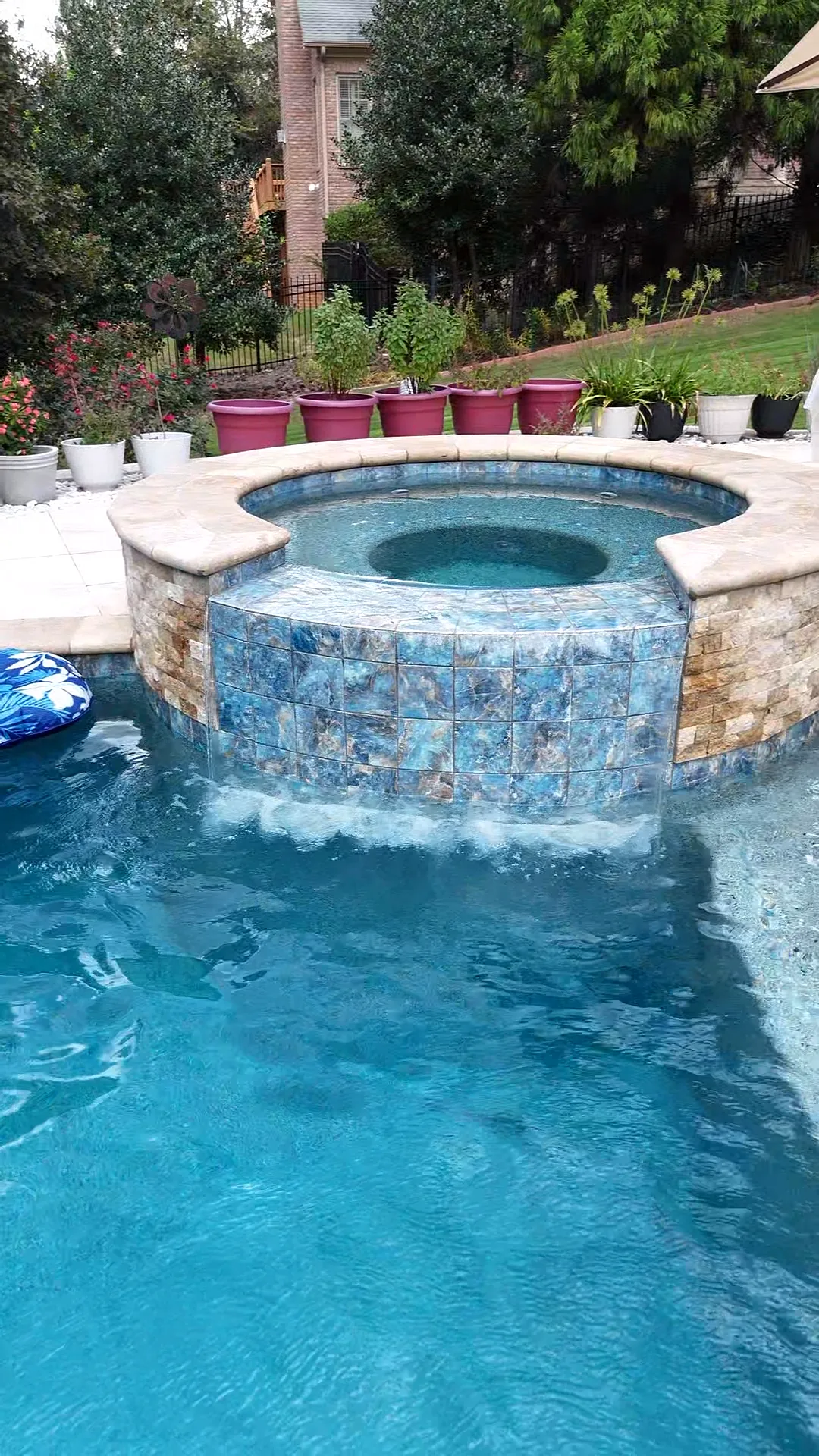 Close view of the Curtis project's round raised spa with blue tile and a spillover flowing into the pool