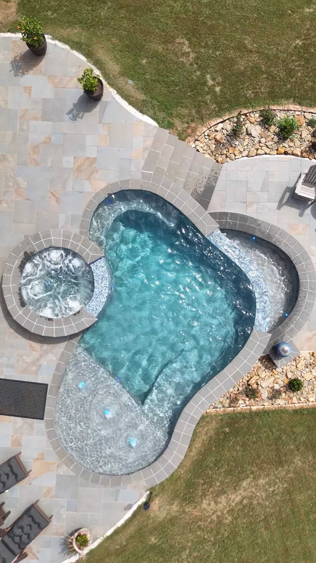 Straight-down aerial view of the finished Talking Rock freeform pool, round raised spa, curved water feature, and surrounding patio