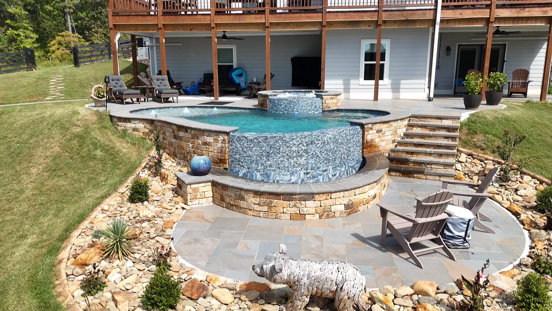 Wide aerial view of the completed Talking Rock pool with a raised spa, curved water feature, stone steps, and patio