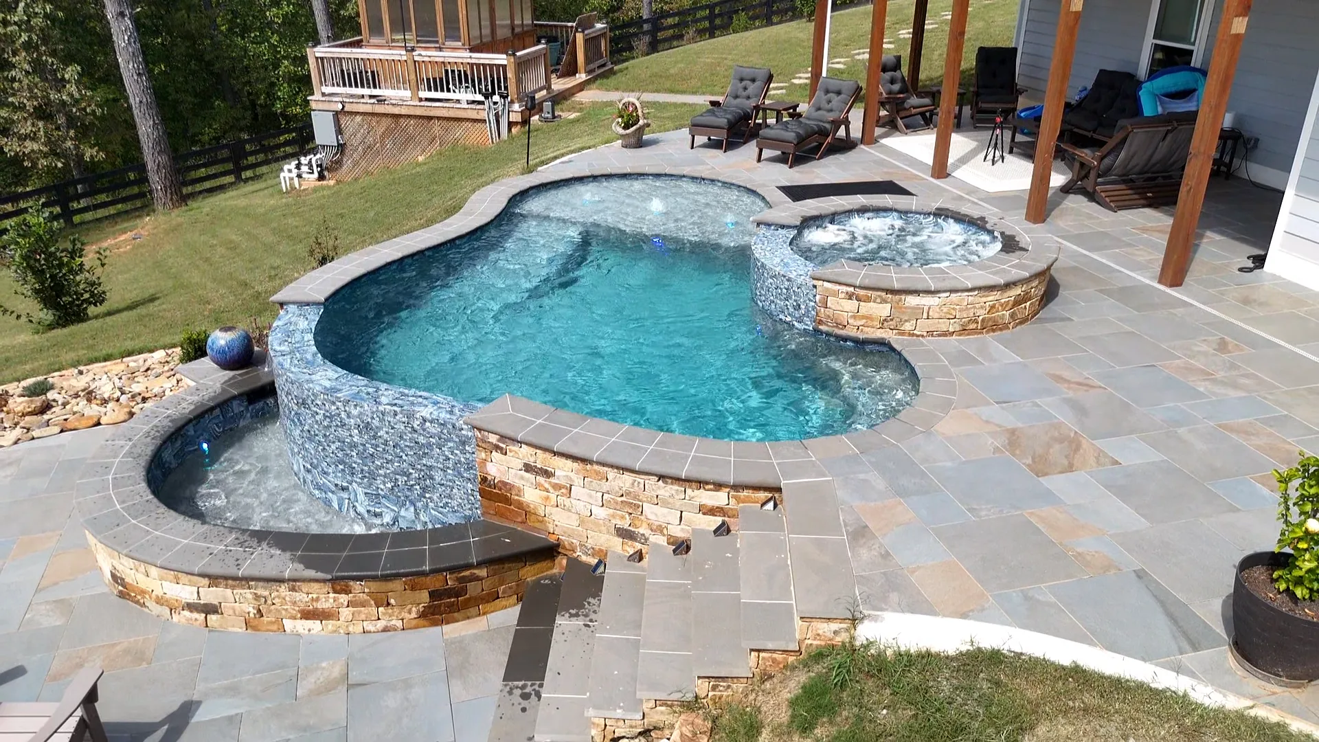 Elevated side view of the Talking Rock pool, round raised spa, curved water feature, and stone patio