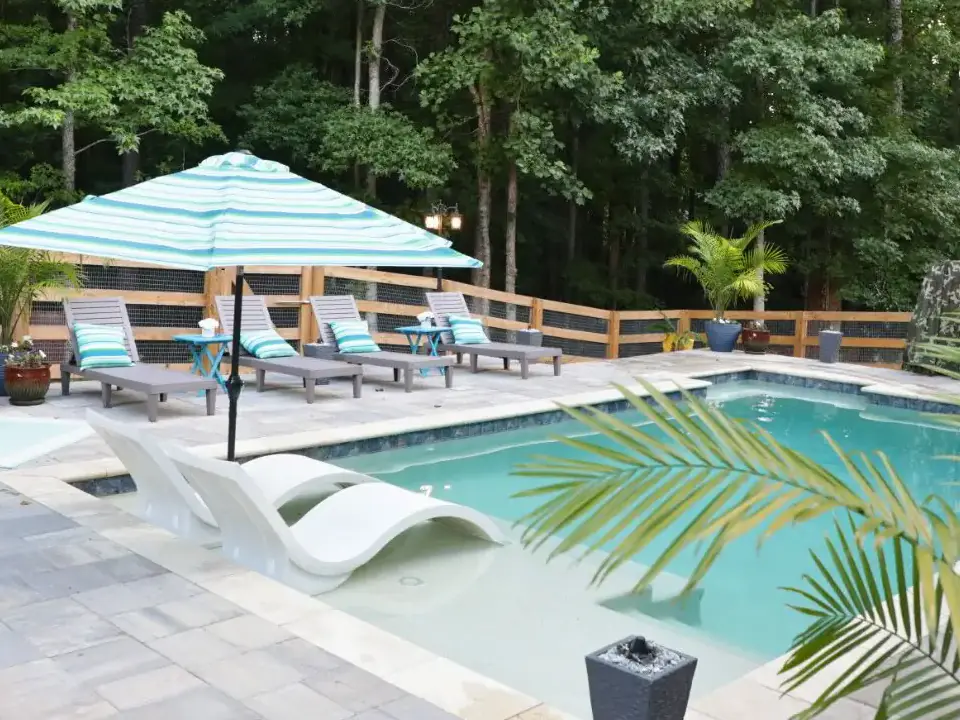 RutherfordMade pool with blue umbrellas, lounge chairs, palm trees, and integrated outdoor living